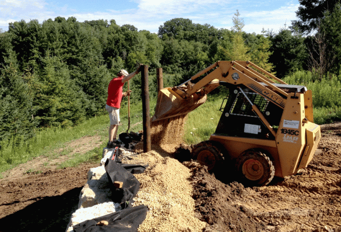 Tom builds walls to last.  (Not like the one these stones were used for previously.)  Doug helped him place landscape cloth against the side of the wall that interfaces with dirt.  Then a generous layer of washed gravel called clear stone was places against the stone.  Now when the soil gets saturated with water and then freezes, the water runs right on through the gravel and does not expand as it freezes - gradually pushing the rocks out of place.